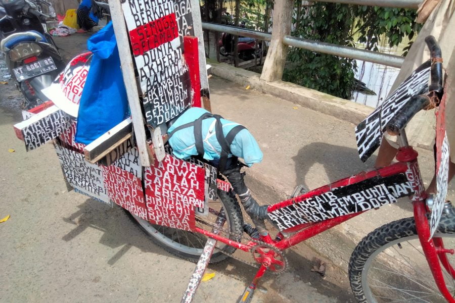 Kakek tua itu memarkir sepeda yang telah ia modifikasi dengan beragam tulisan serta dicat merah. (Foto/Hae)